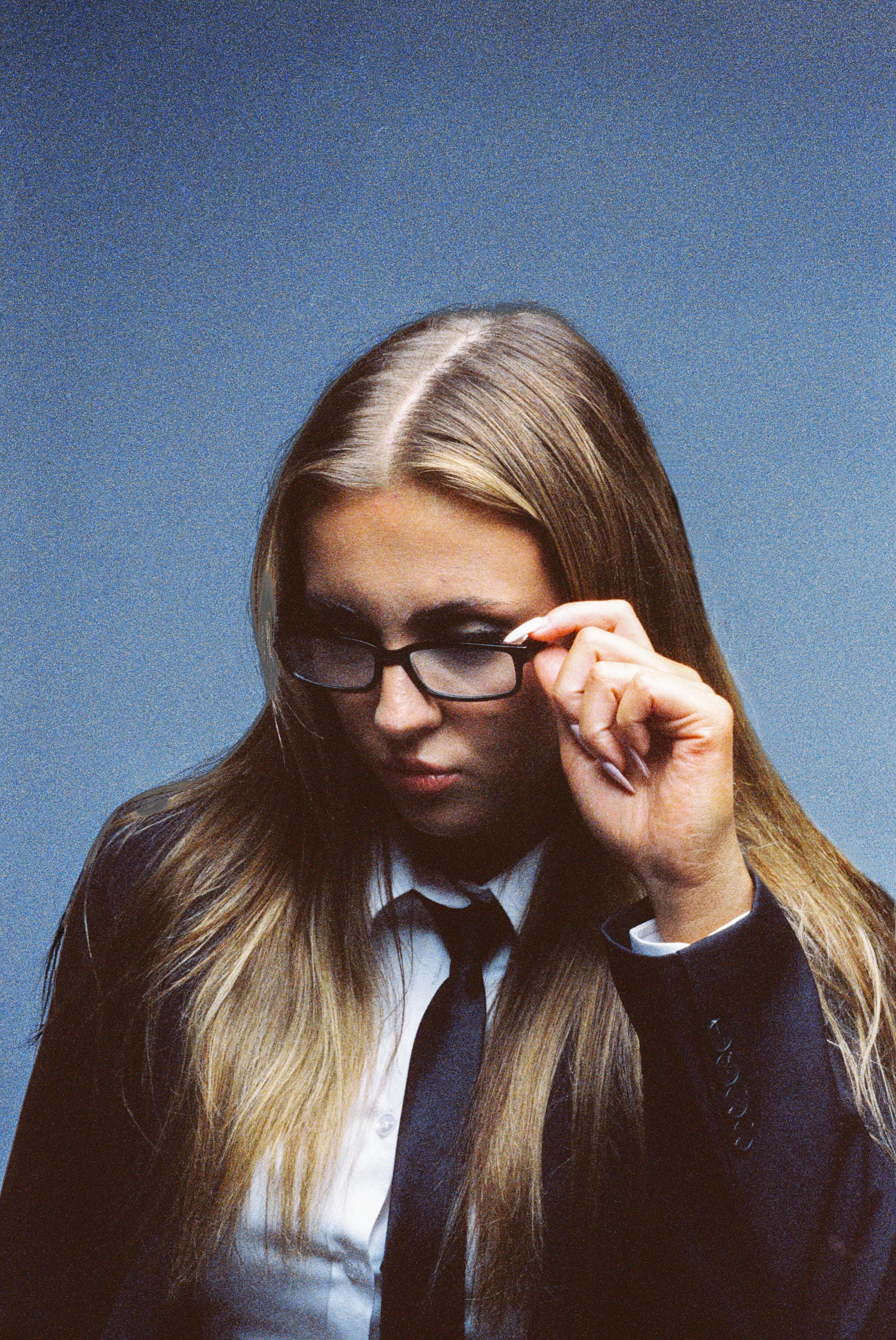 Film portrait of a woman in glasses and a tie against a blue backdrop.