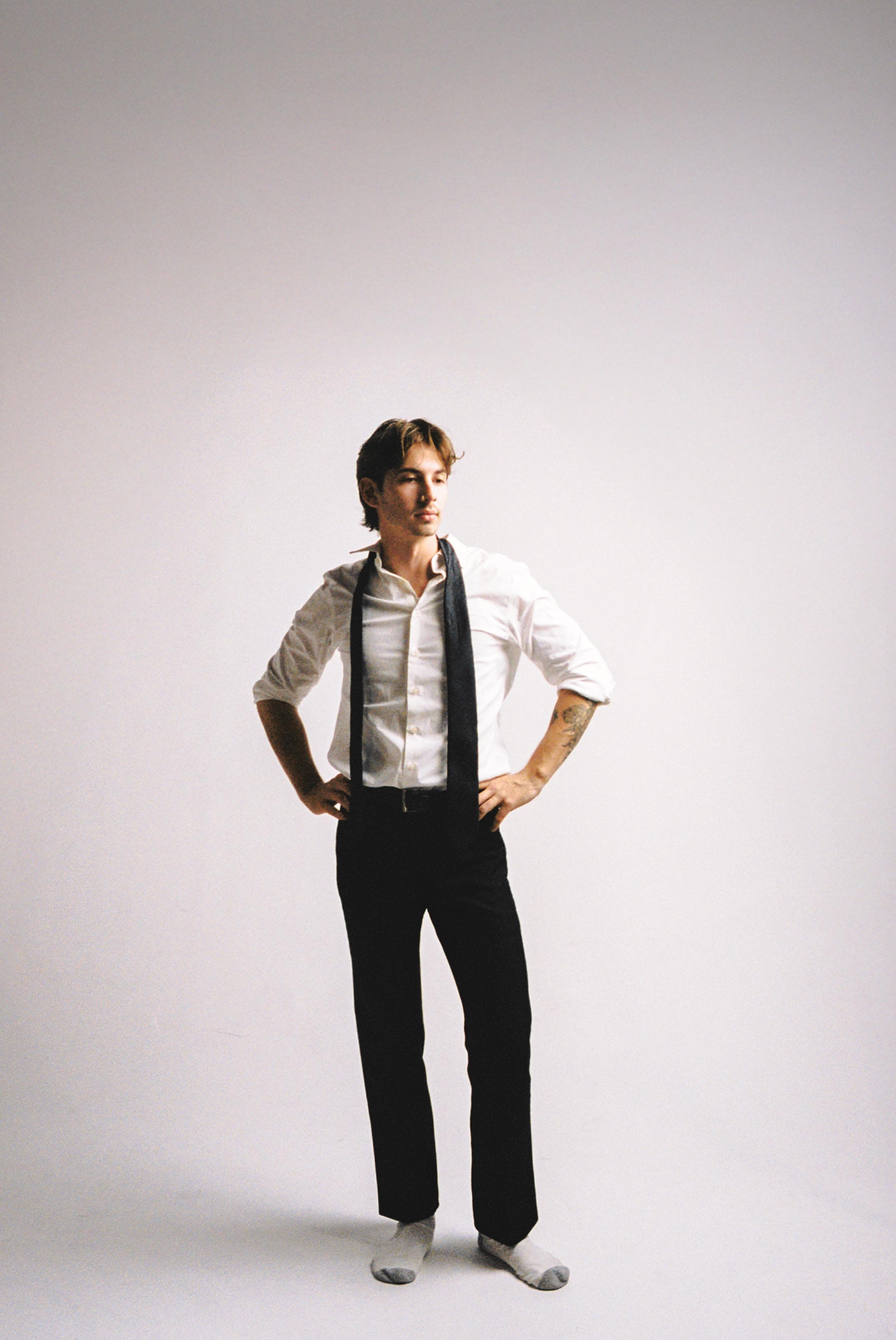 Full-length film portrait of a man in a white shirt and tie on a white backdrop.