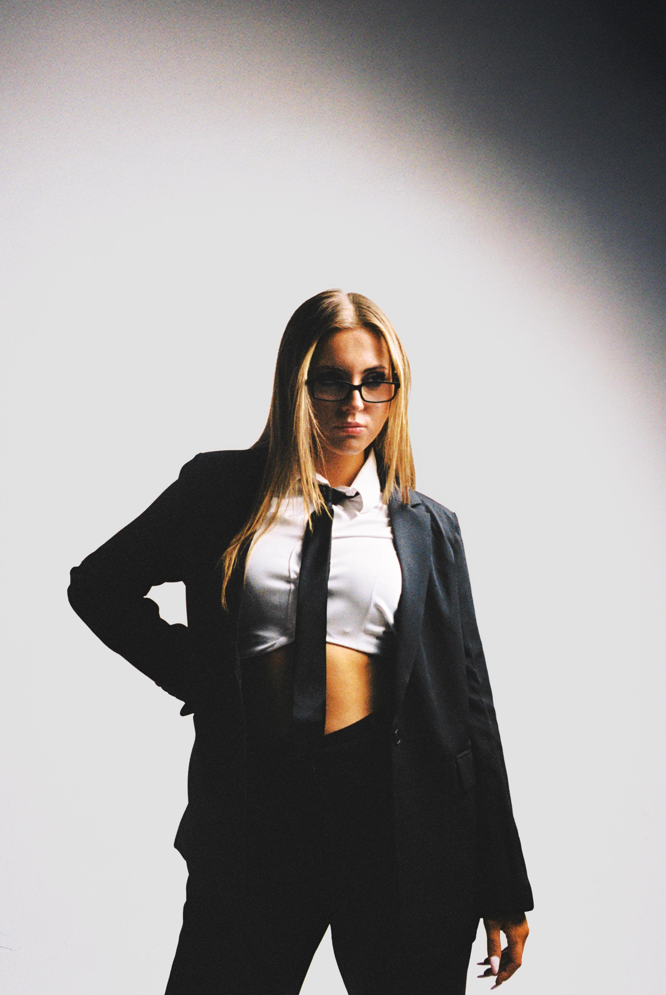 Film portrait of a woman in a black suit and sunglasses under a spotlight.