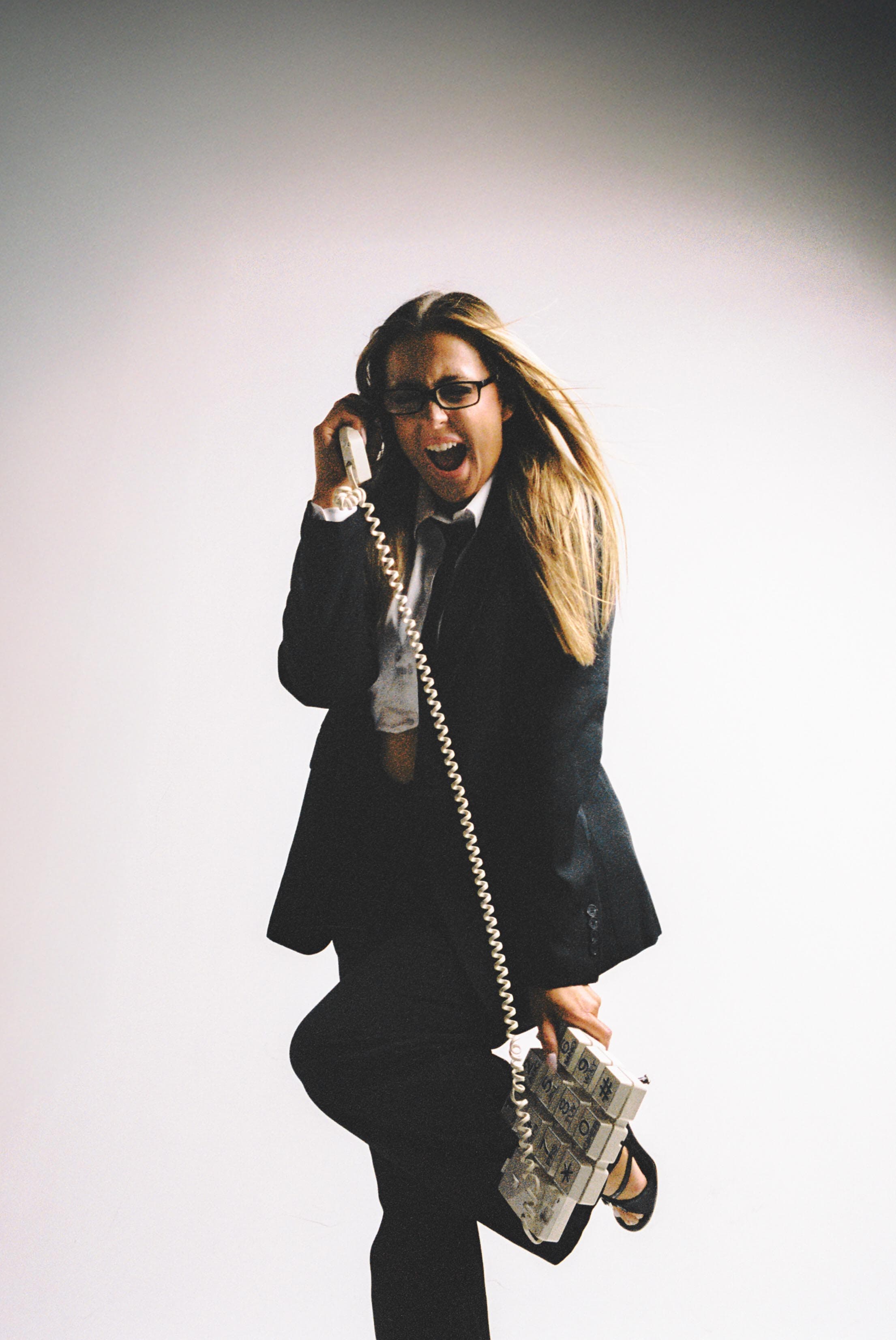 Woman in a black suit laughing into a corded phone.