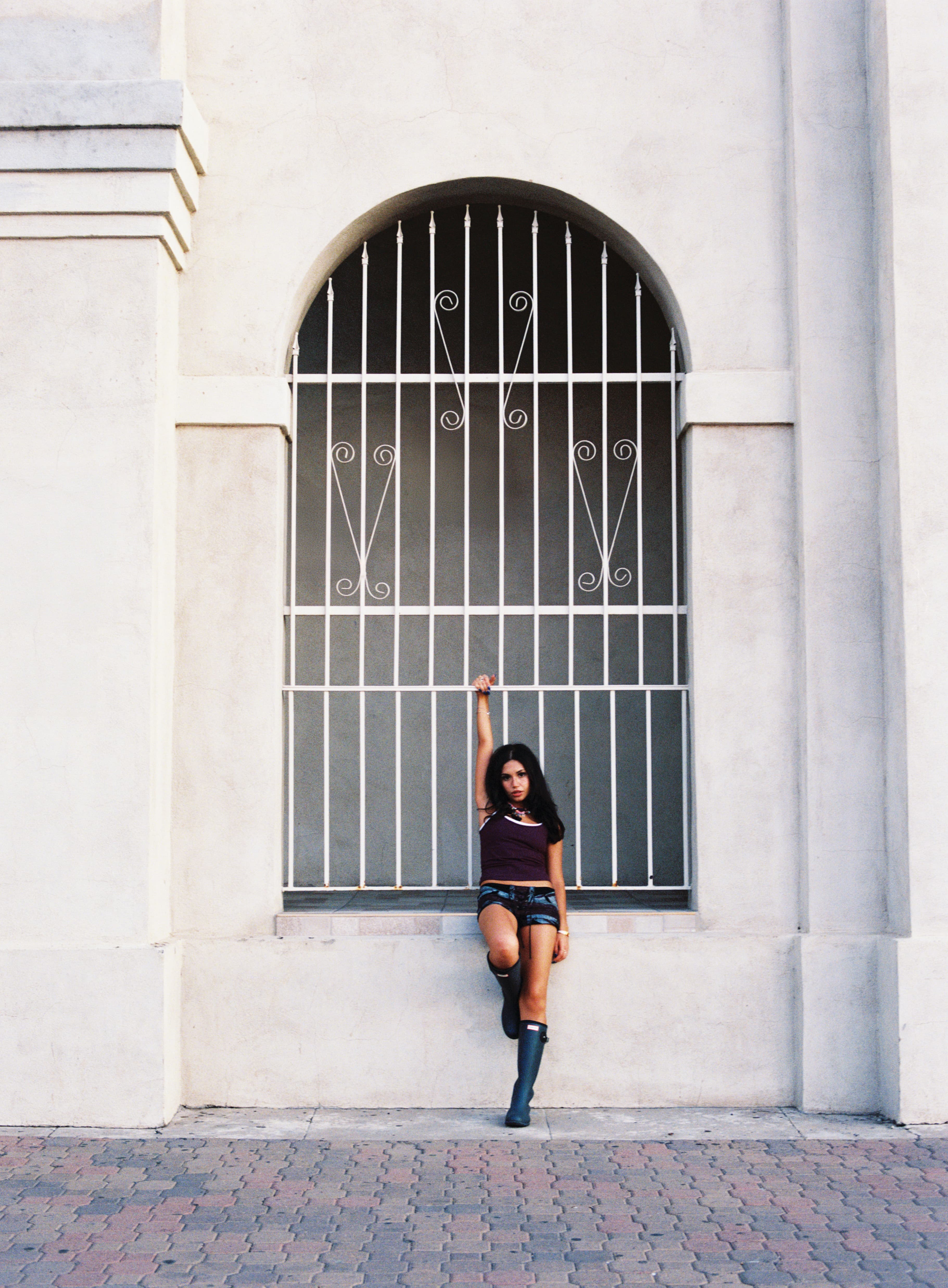 Woman posing in an arched, barred window of a white building.