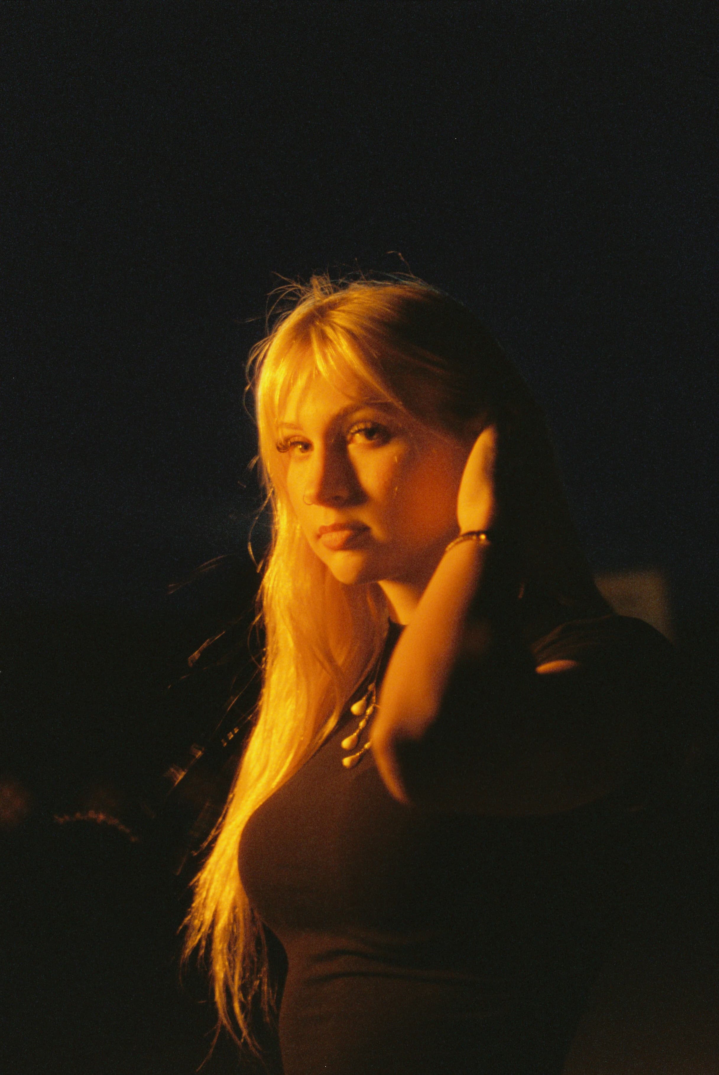 Woman lit in warm orange light against a dark background.