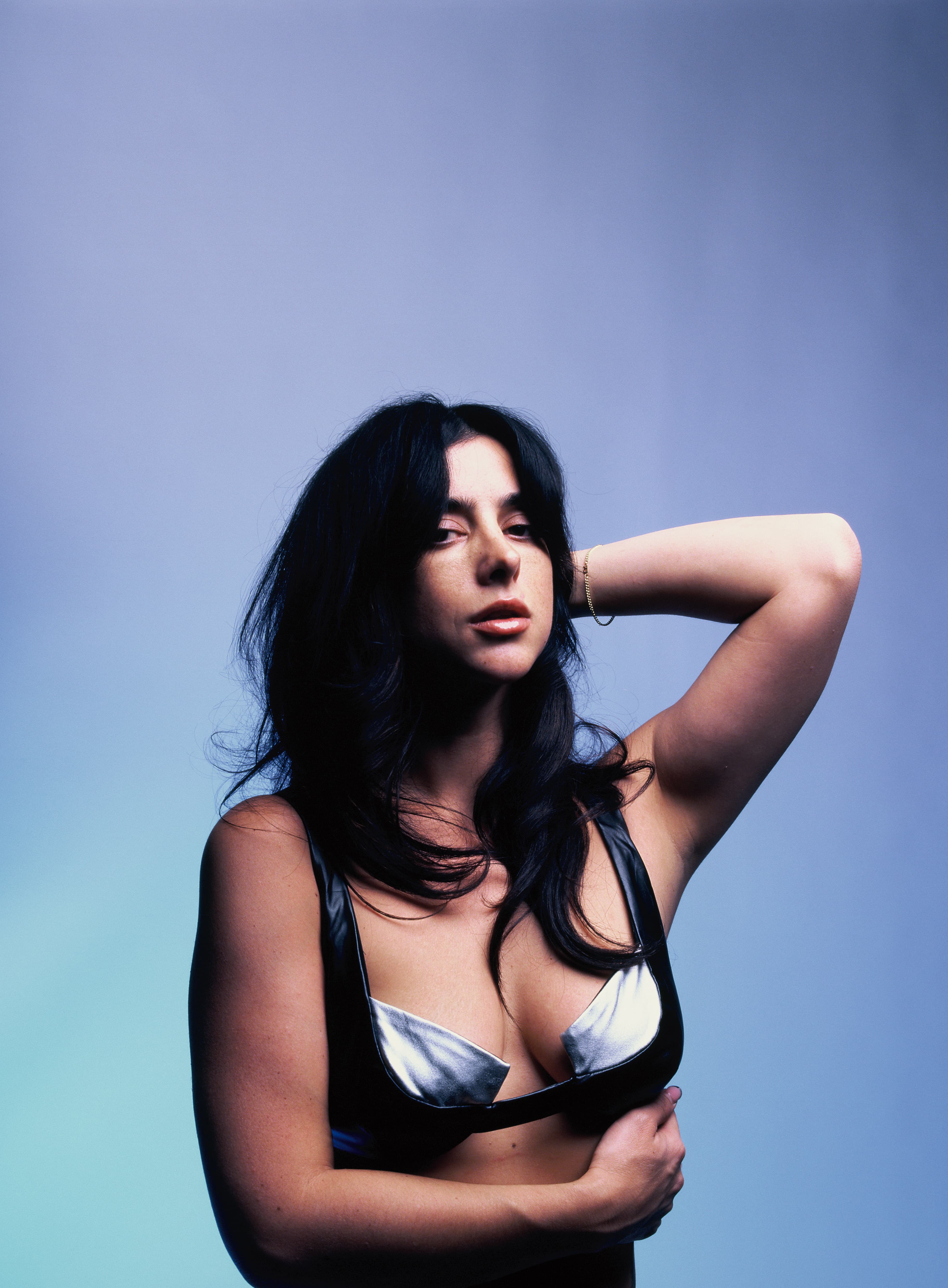 Studio portrait of a woman in a metallic bra top against a blue backdrop.