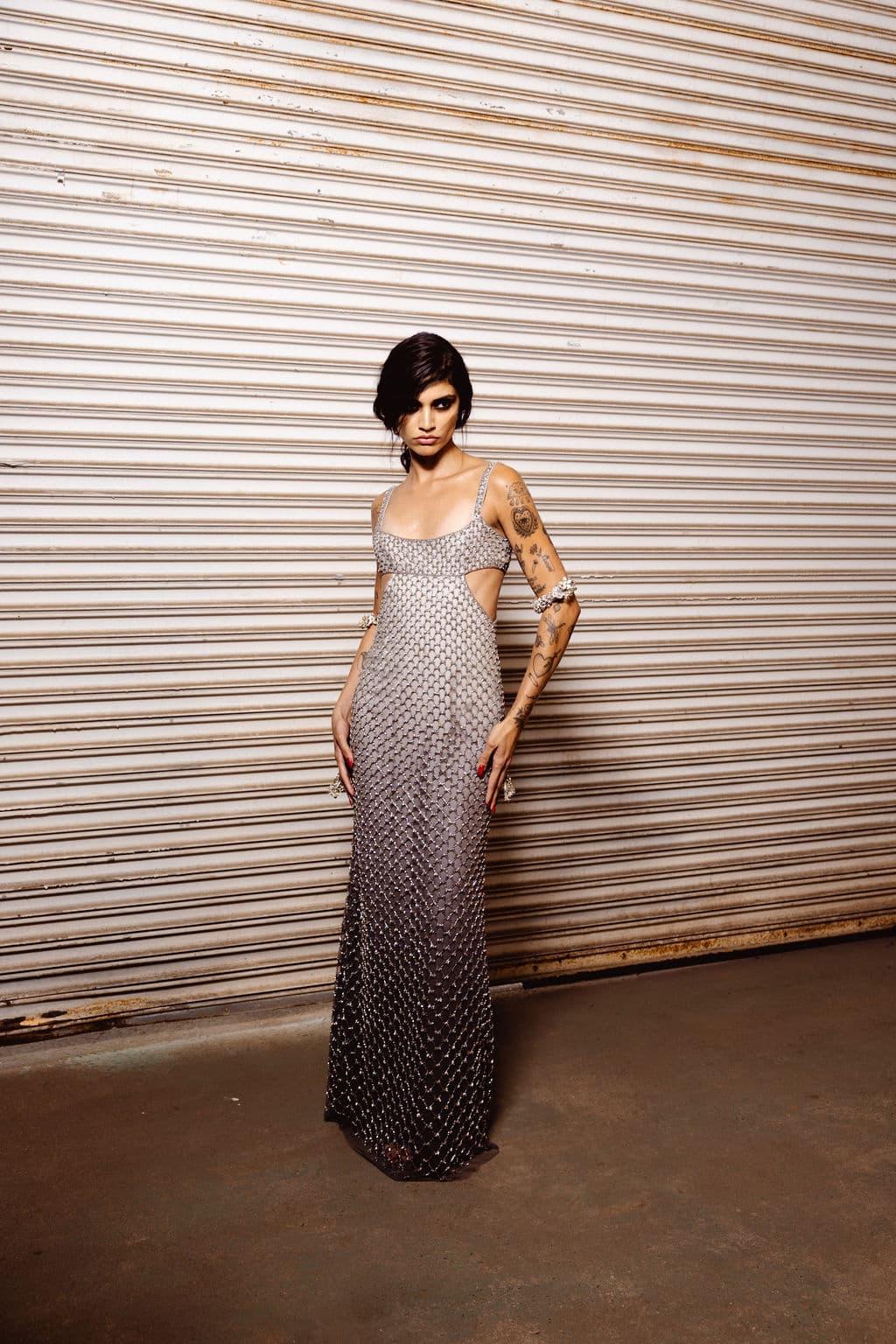 Model in a floor-length silver mesh dress before the runway.