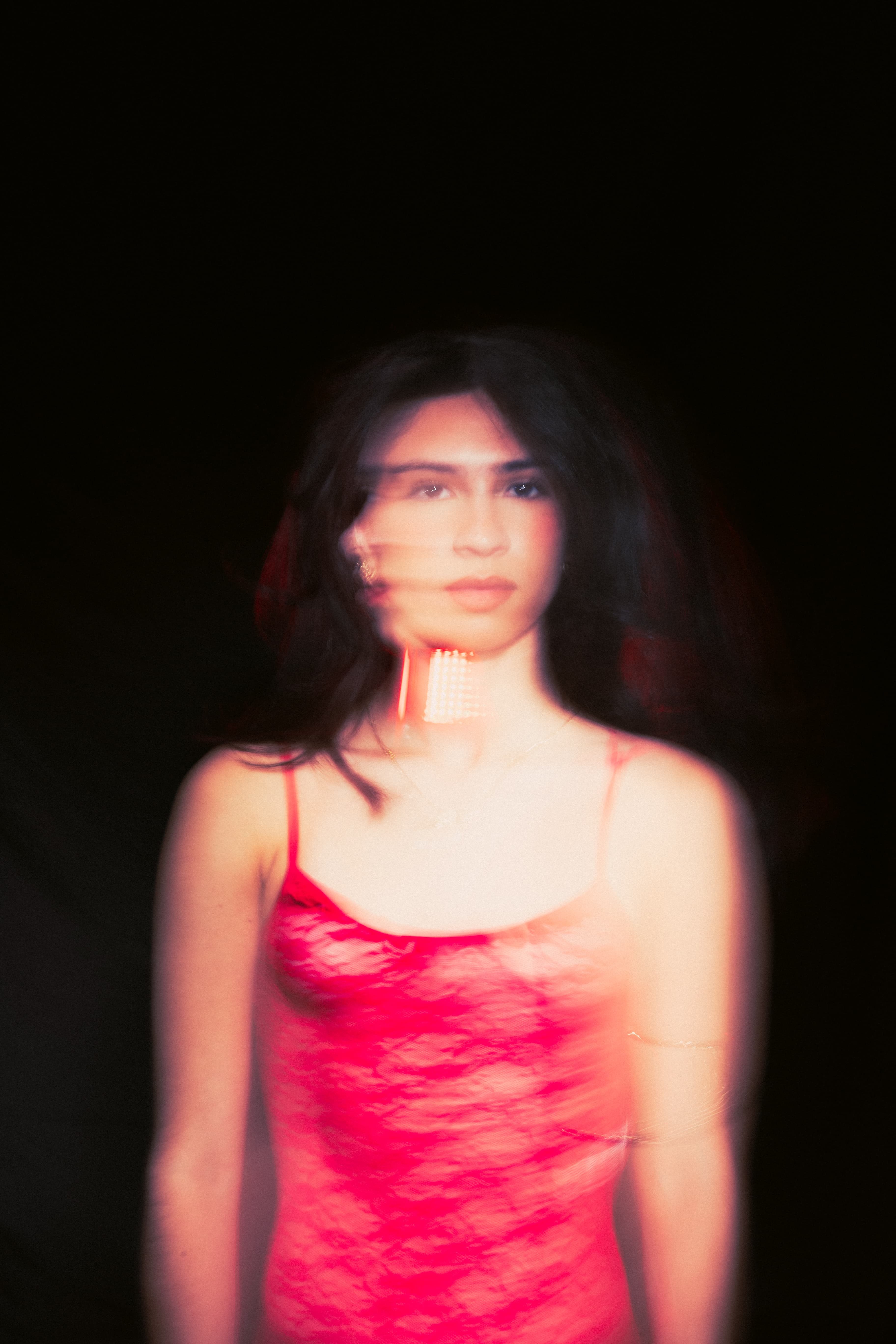 Motion-blurred portrait of a woman in a red lace slip against black.