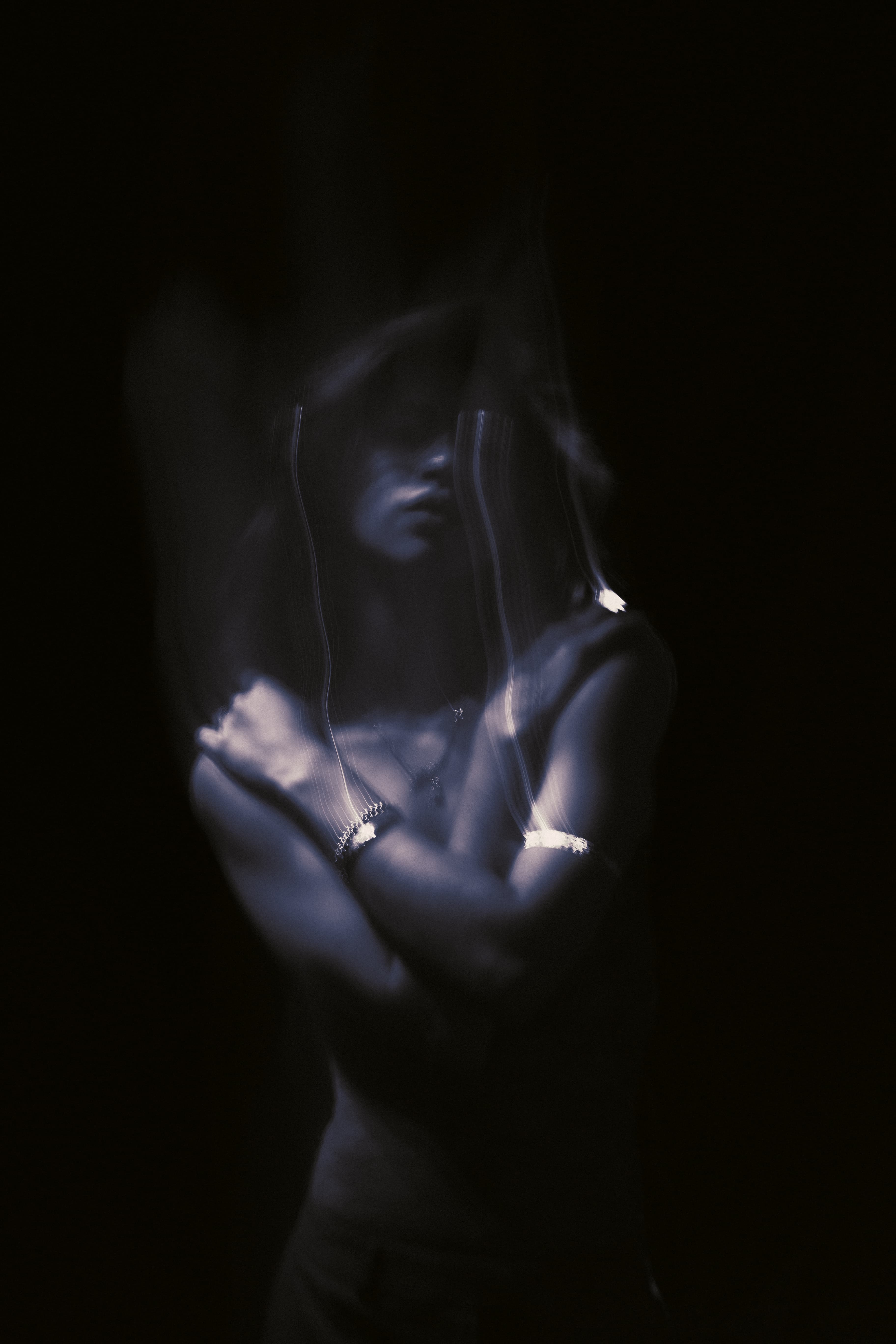 Low-light portrait of a woman with crossed arms, lit in cool blue.