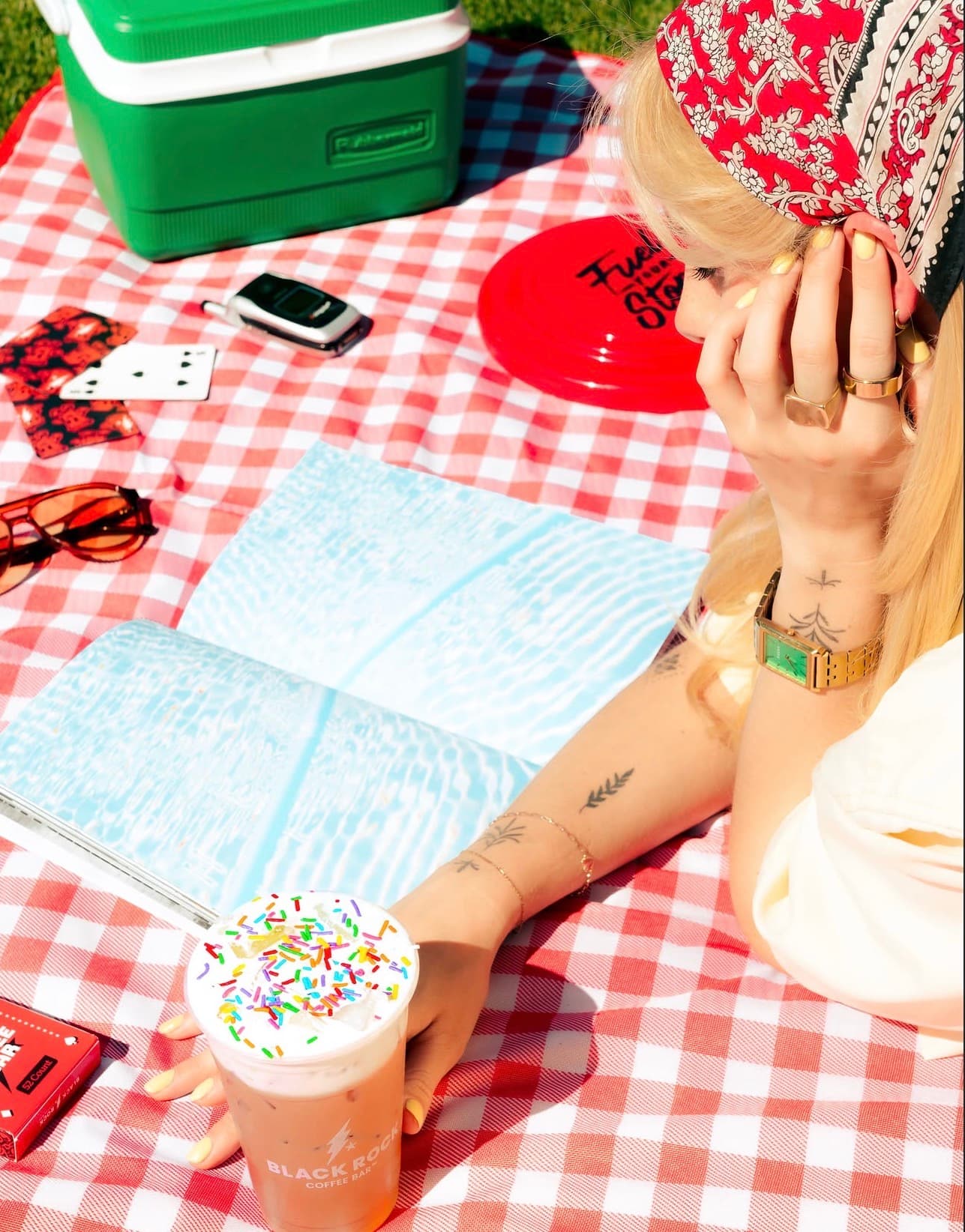 Hannah Warren with a Black Rock Coffee Bar drink at a colorful picnic setup.