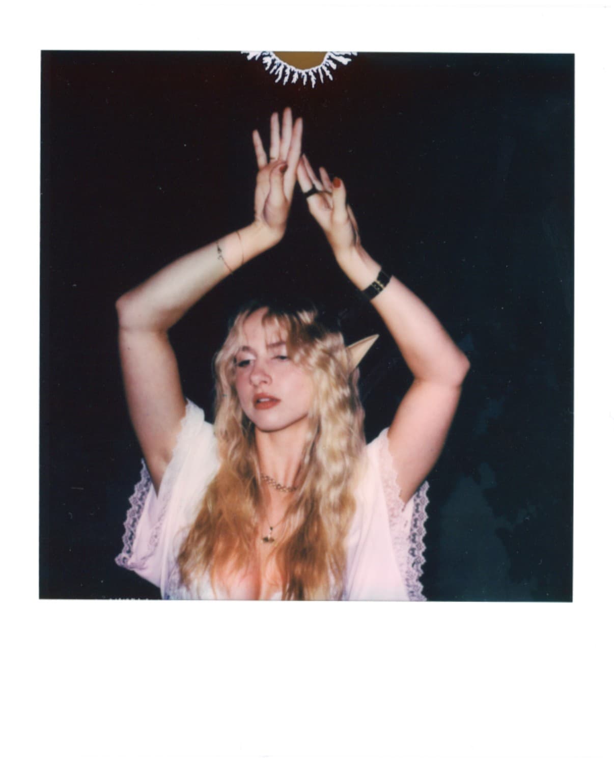 Polaroid of a woman with elf ears raising her hands overhead.