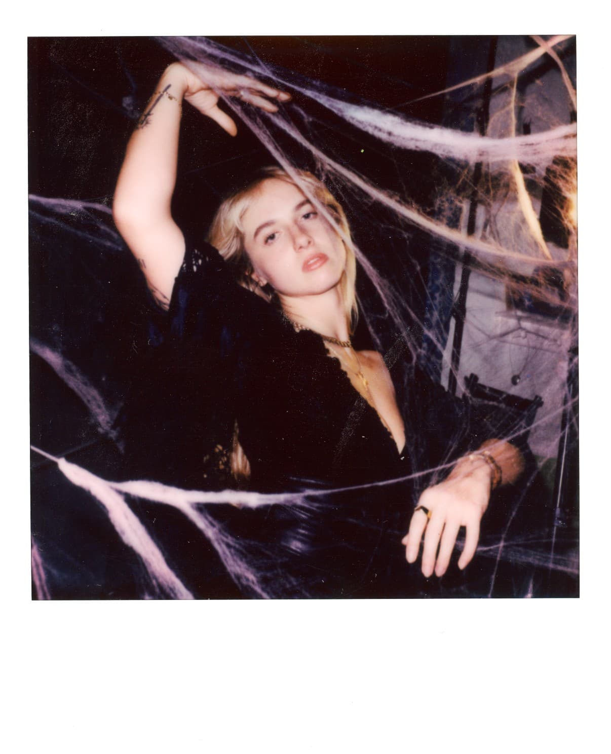 Polaroid of a woman in black among cobweb decorations.