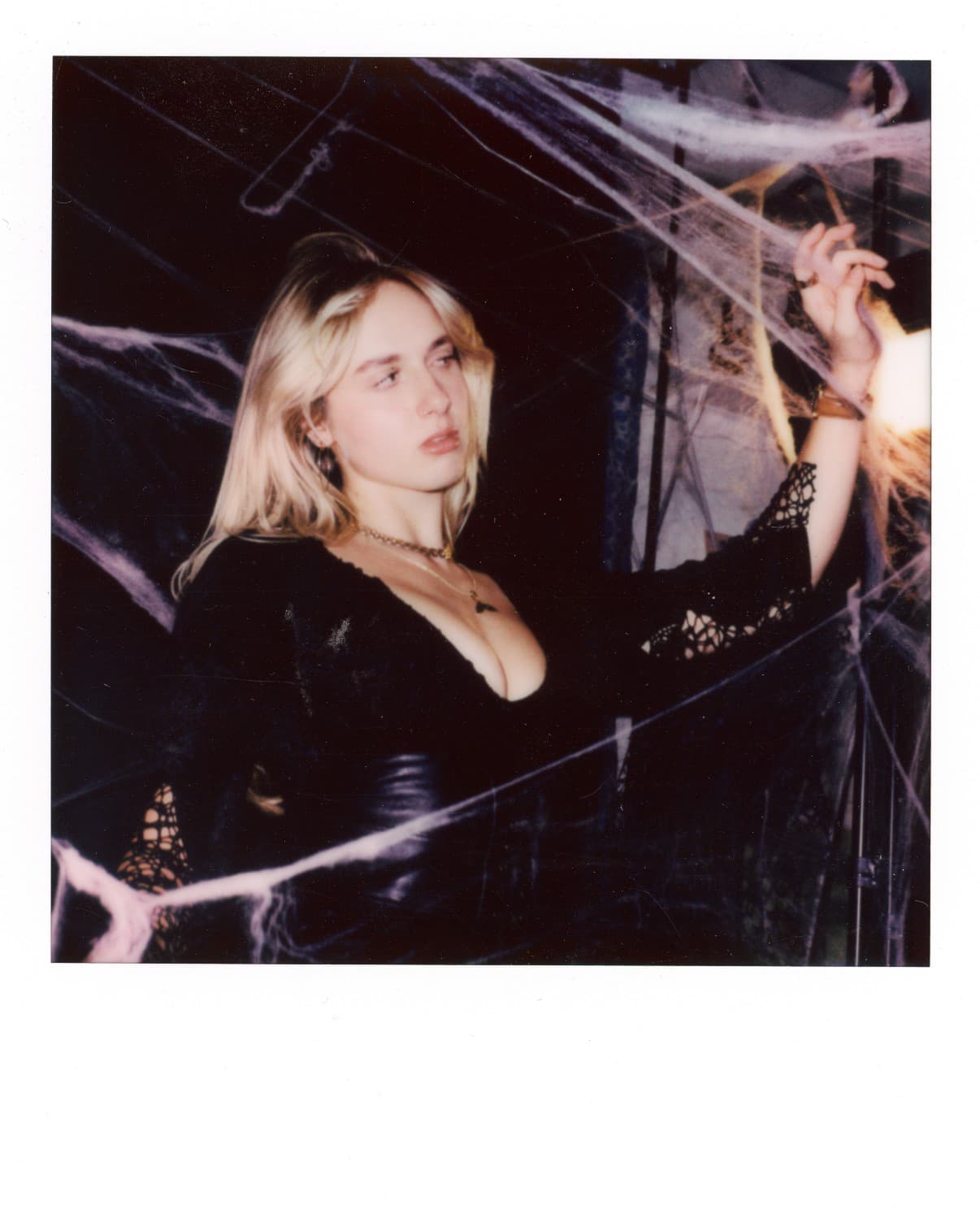 Polaroid of a woman in black posing with cobwebs.