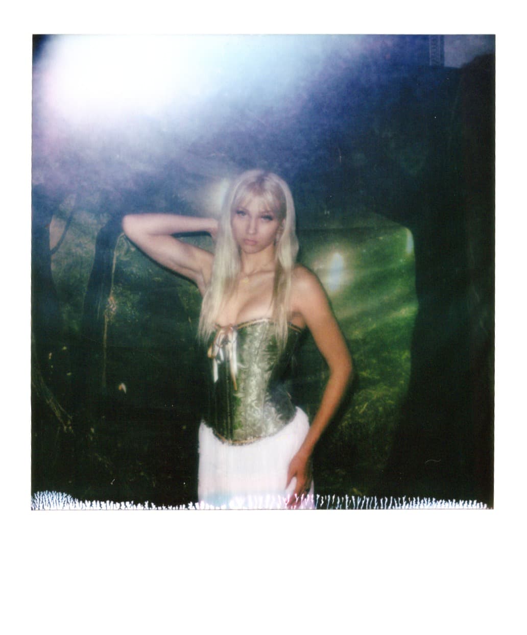 Polaroid of a woman in a corset with one hand raised to her hair.