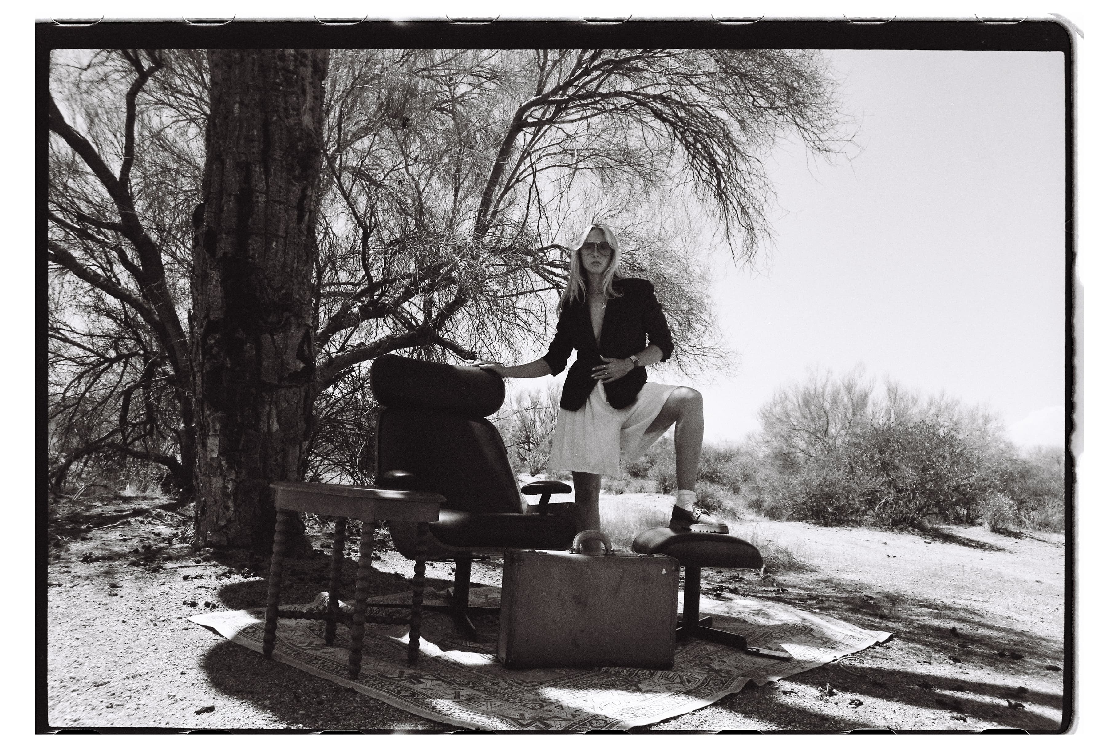 Black-and-white self-portrait of Hannah Warren staged outdoors with vintage furniture.